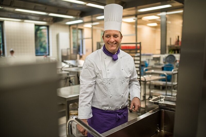 Ein lächelnder Koch steht in einer Großküche.