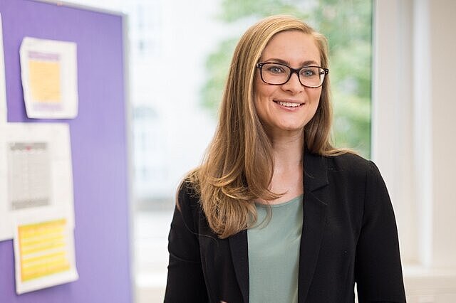 Mitarbeiterin in der Verwaltung steht lächelnd neben einer Pinwand.